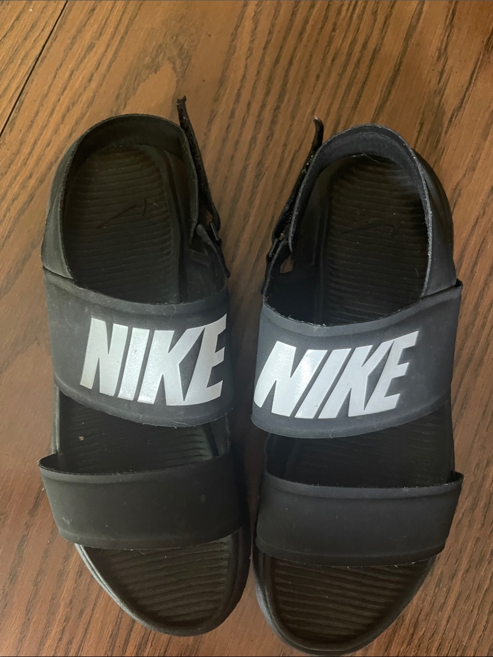 black and white Nike Tanjun sandals sfeaturing a prominent "NIKE" logo on the st